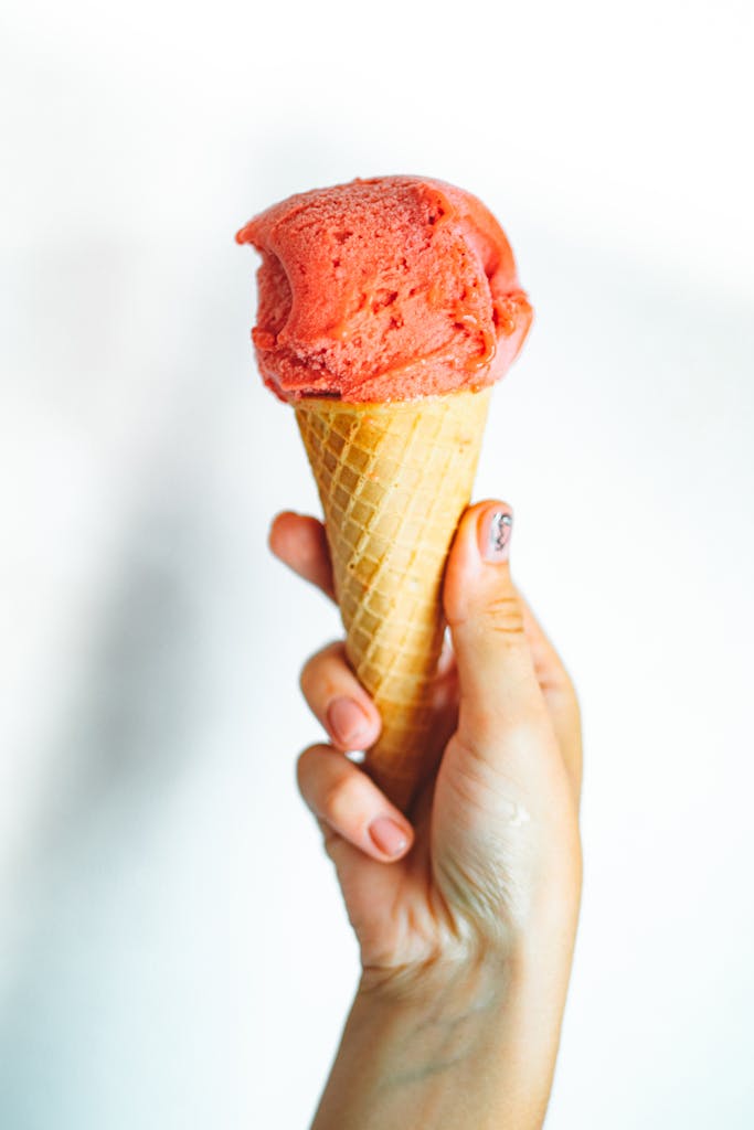 Close-up of a hand holding a strawberry ice cream cone against a white background.