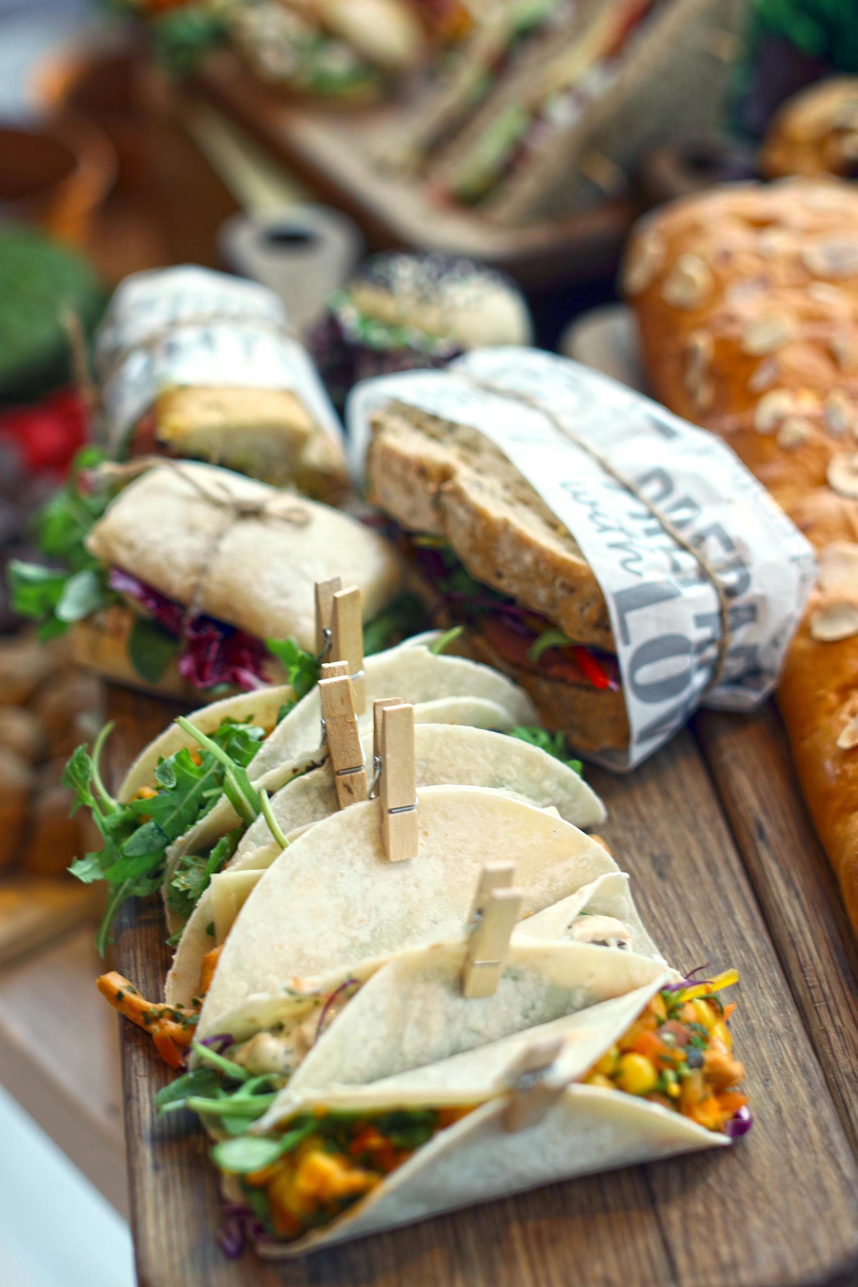 Close-up of assorted fresh tacos and sandwiches on a rustic wooden board with vibrant garnishes.
