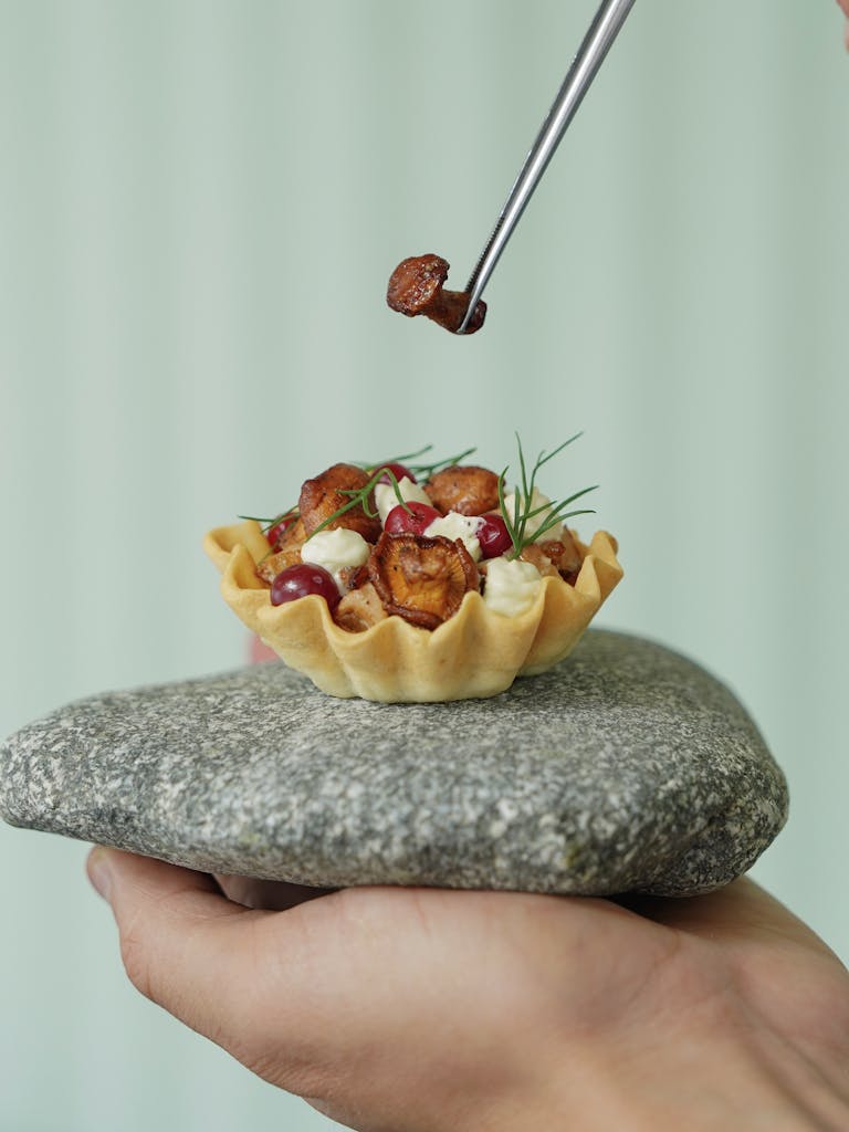 Fresh gourmet tartlet being garnished by hand, displayed on stone for a modern presentation.