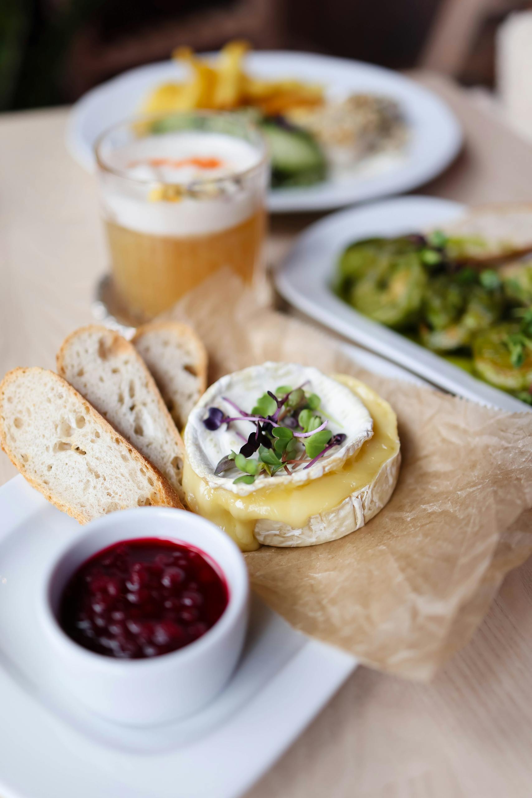 Melted Brie cheese on parchment with bread, berry compote, and fresh greens.
