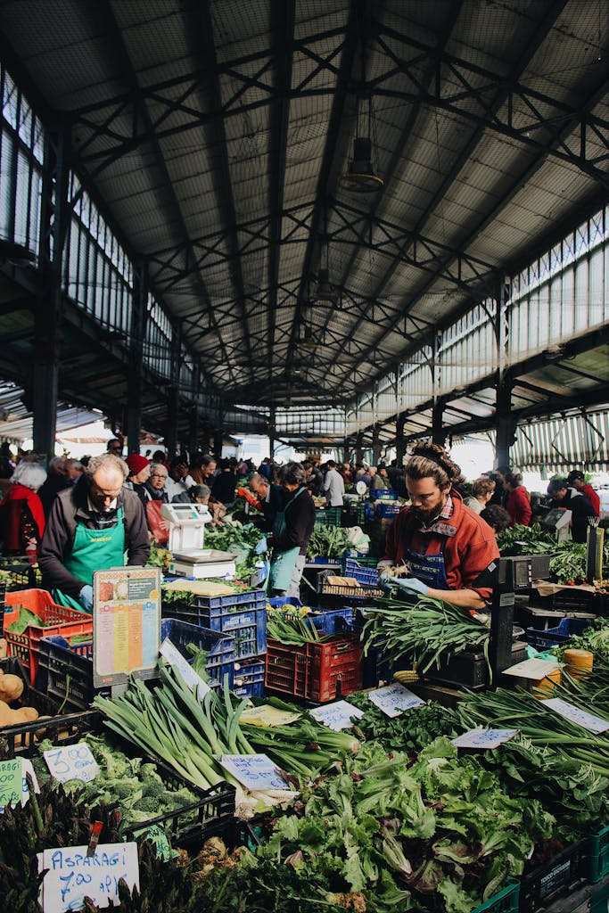 Indoor farmers market bustling with people buying fresh vegetables from vendors.