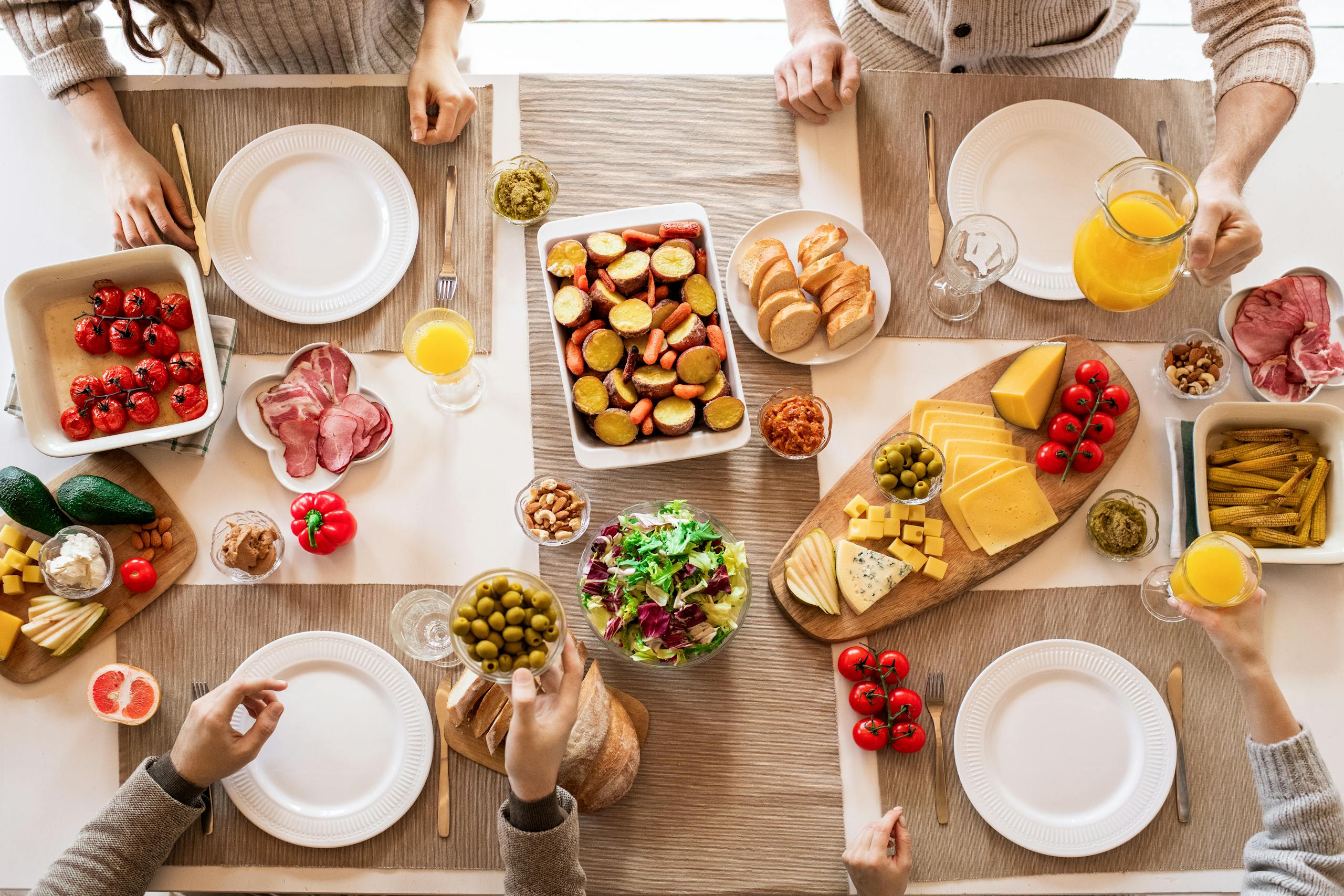 Overhead view of a lively brunch setup with assorted foods, cheeses, and juices on a table.